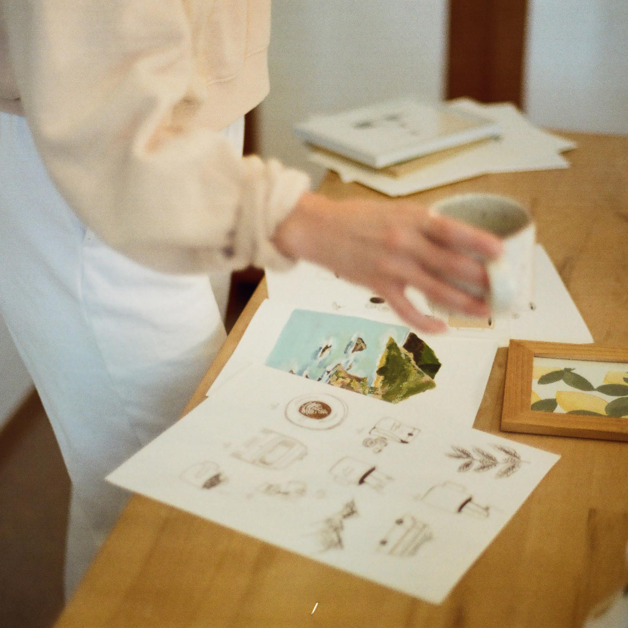 women sorting various works of art on the table while holding a coffee cup