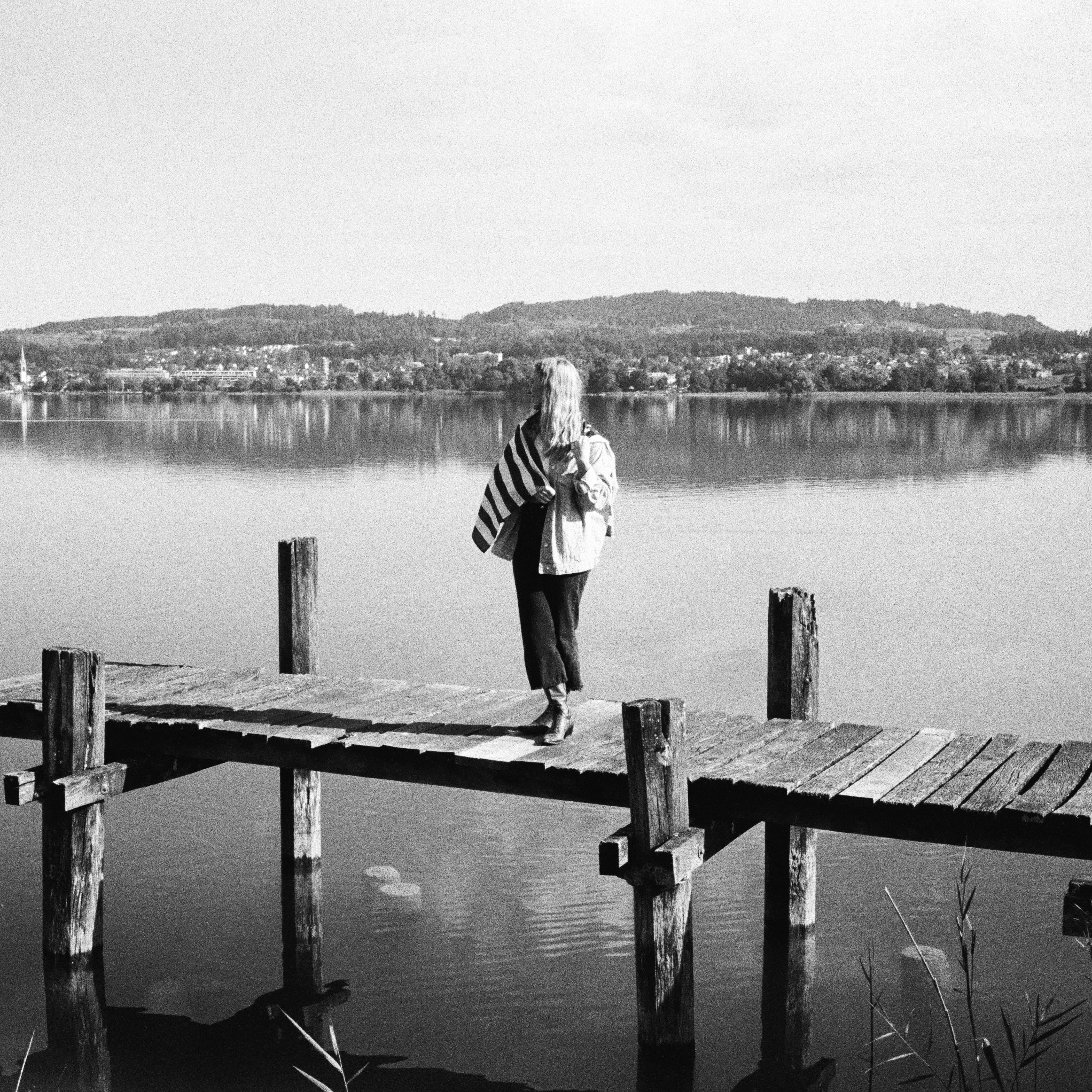 woman standing on a pier at a lake while carrying an American flag over her shoulder