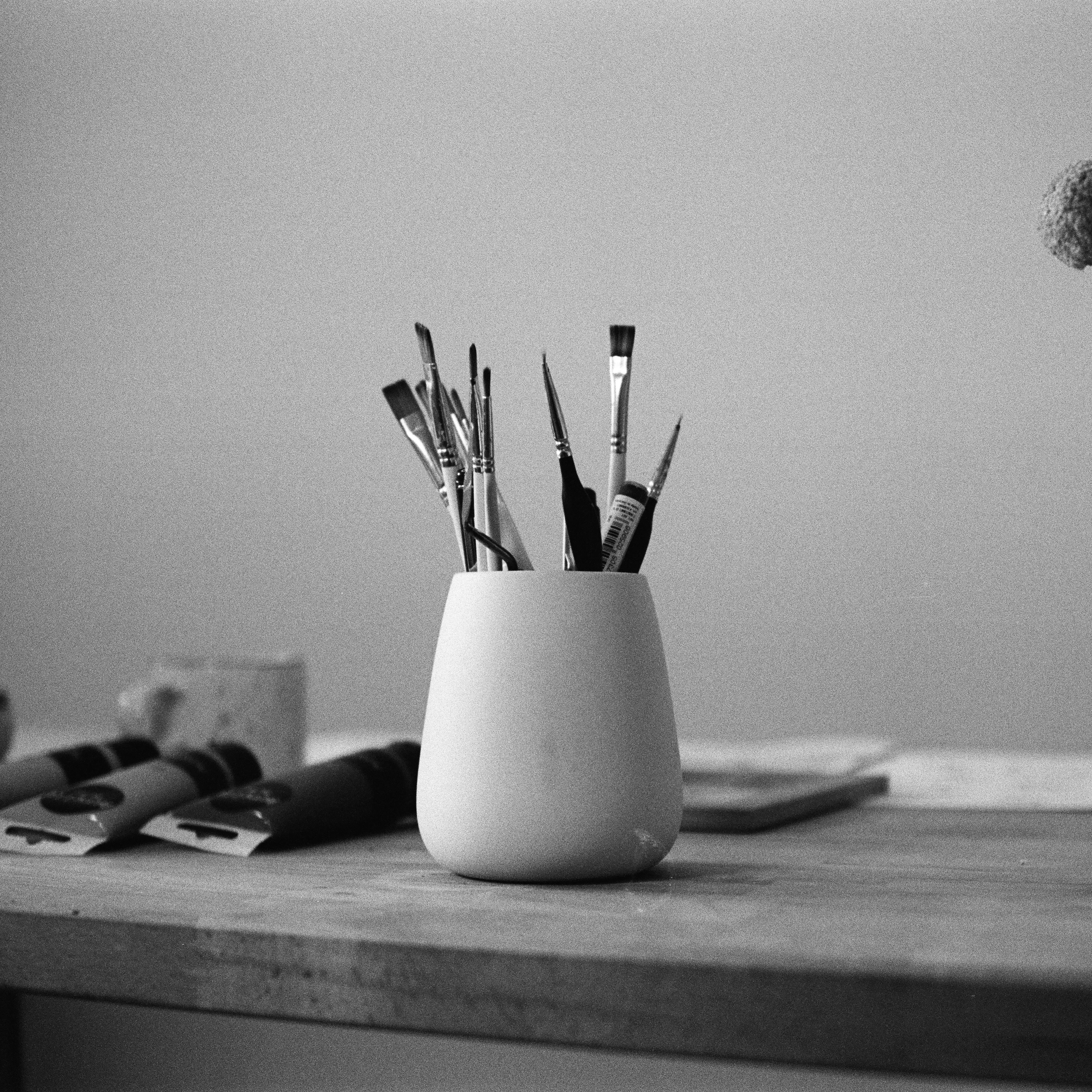 table with a vase and various brushes in it and tubes of paint lying next to it