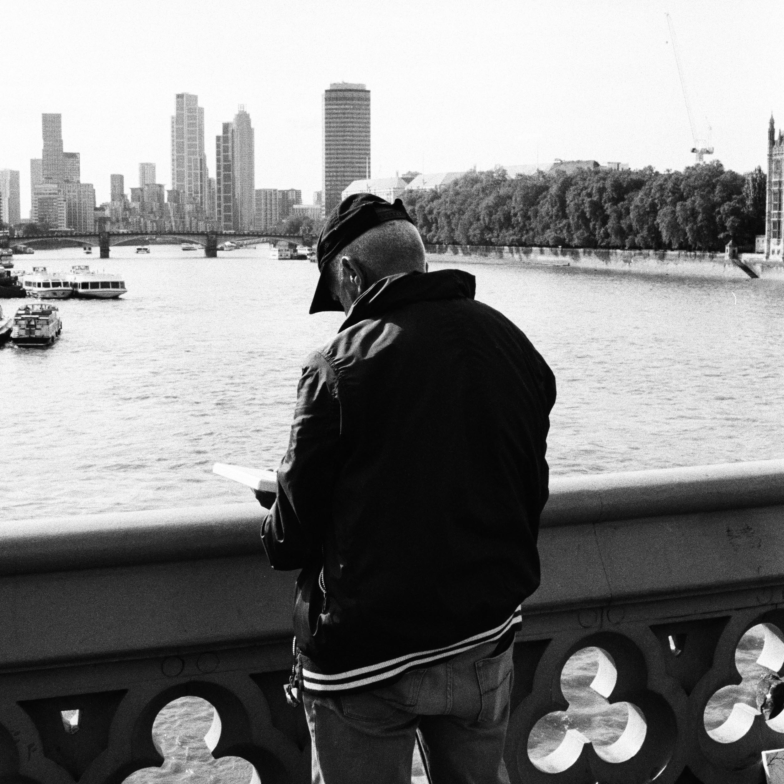 man stands on a bridge over the Thames and draws a work of art