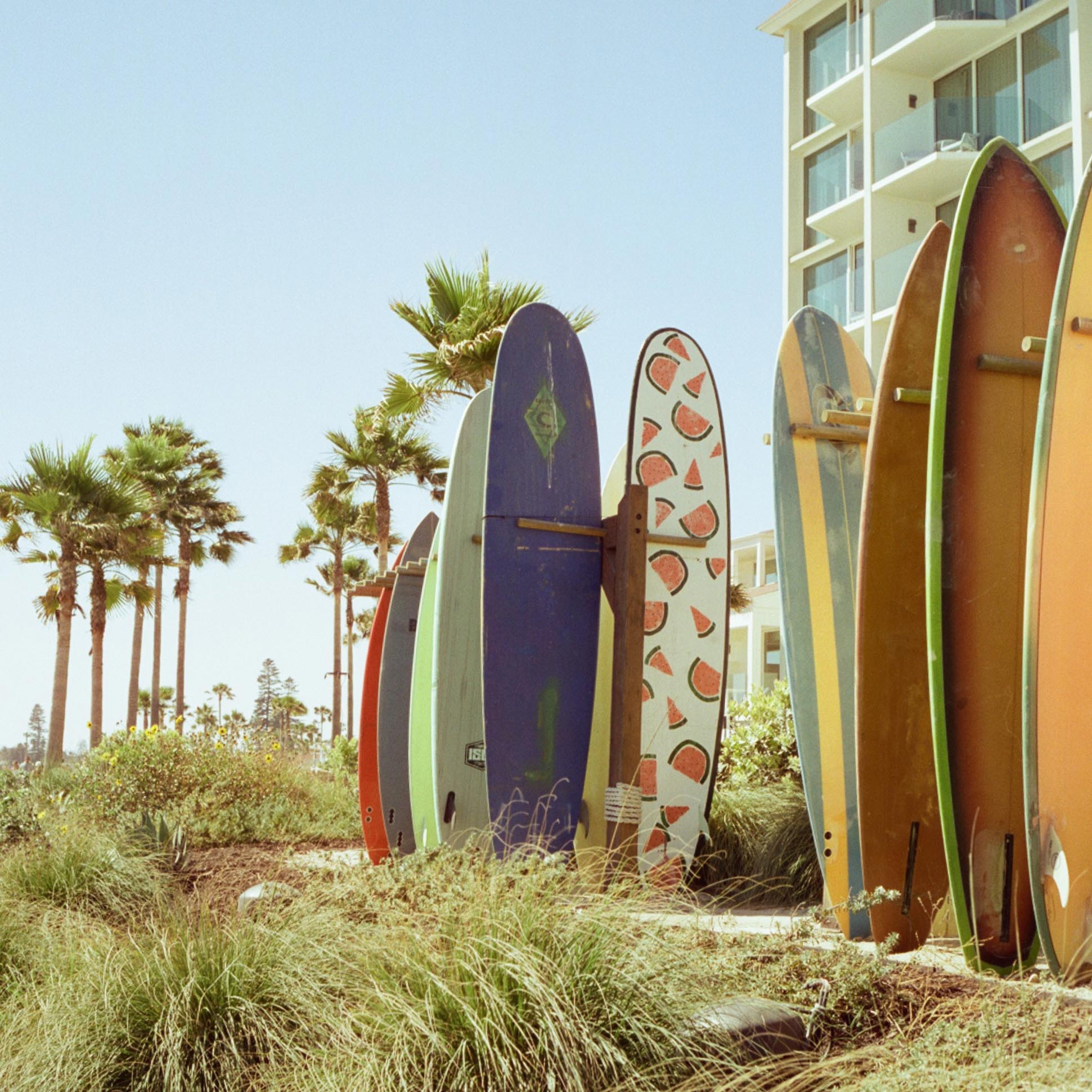 stacked surfboards in front of a hotel with palm trees in the background
