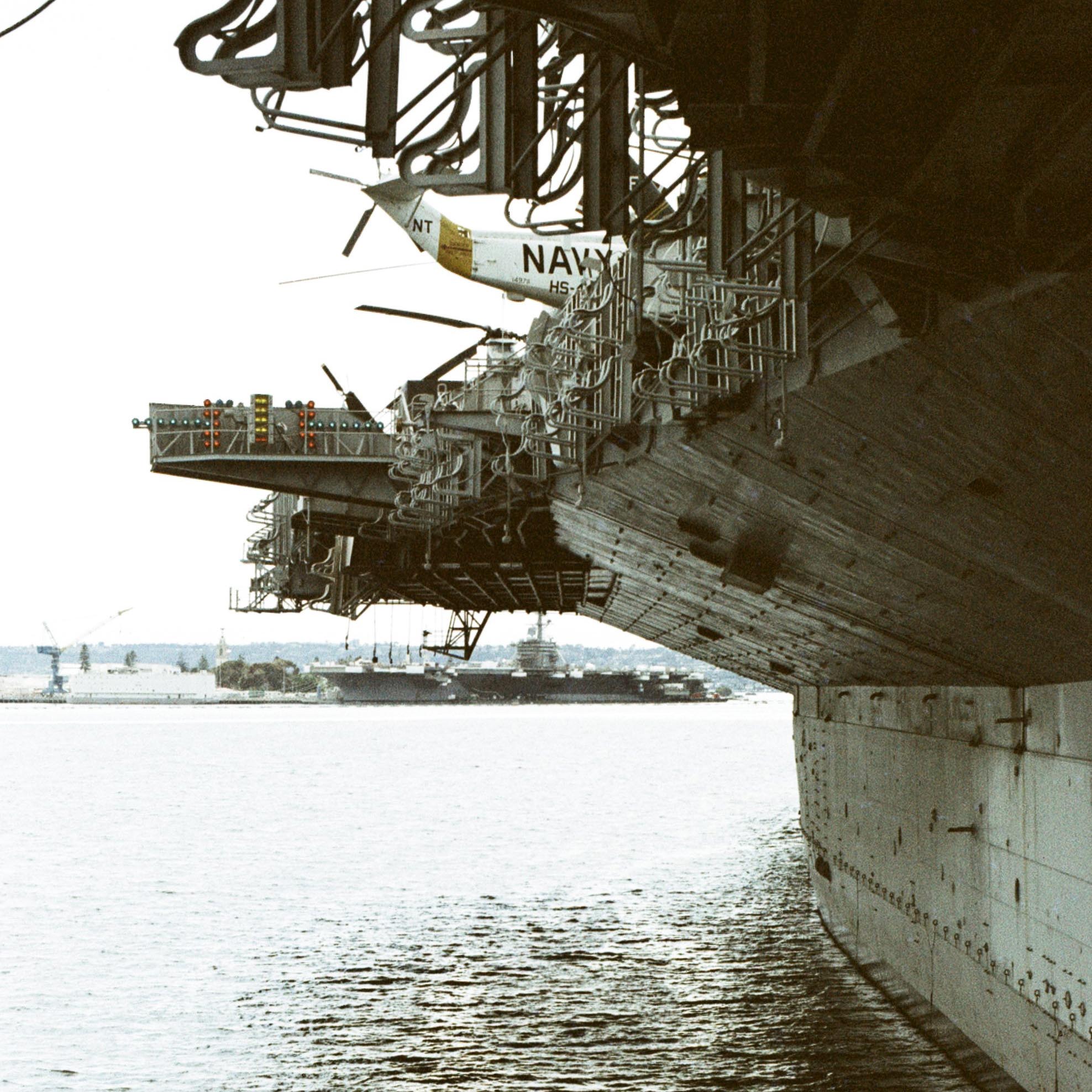 side of an aircraft carrier with another aircraft carrier in the background