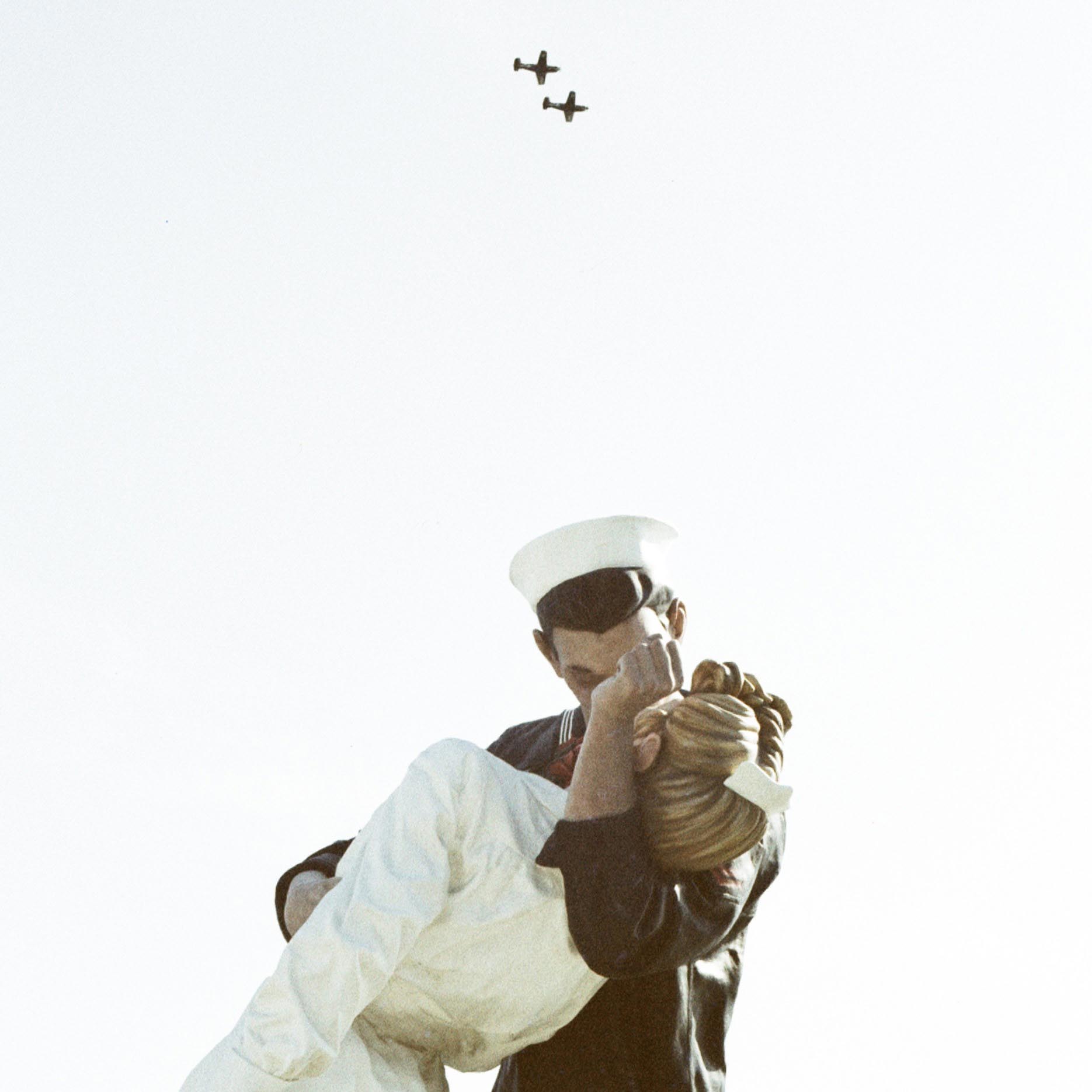 kissing statue with two old WW2 planes flying over it in formation