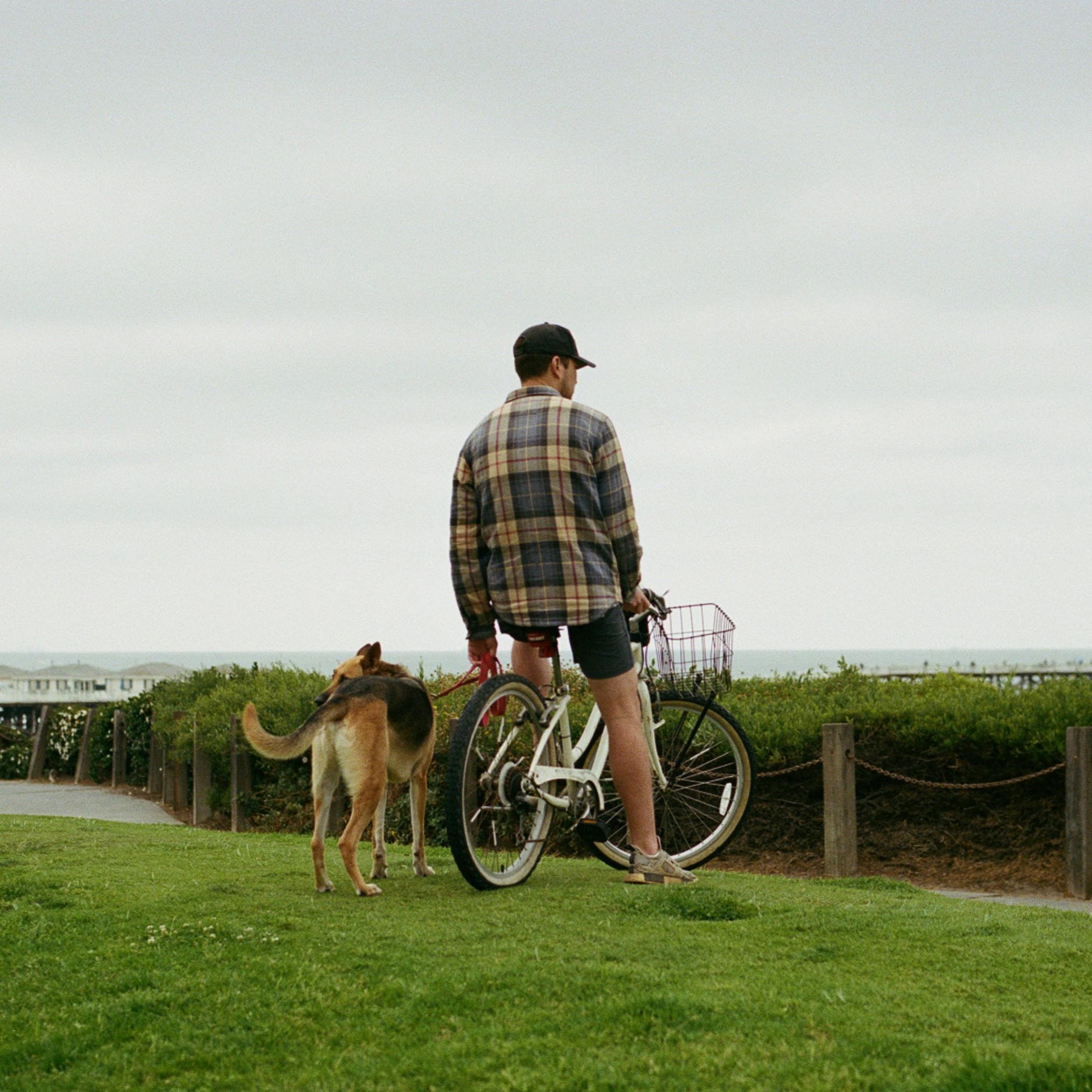 man sitting on a bicycle overlooking the sea with his dog beside him