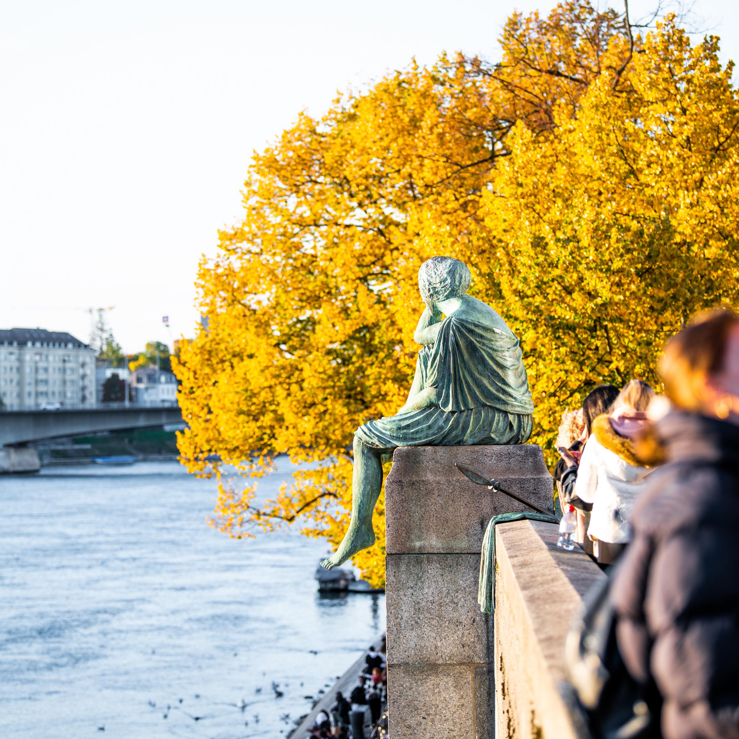 seated statue of a woman looking at a river with autumn colored trees