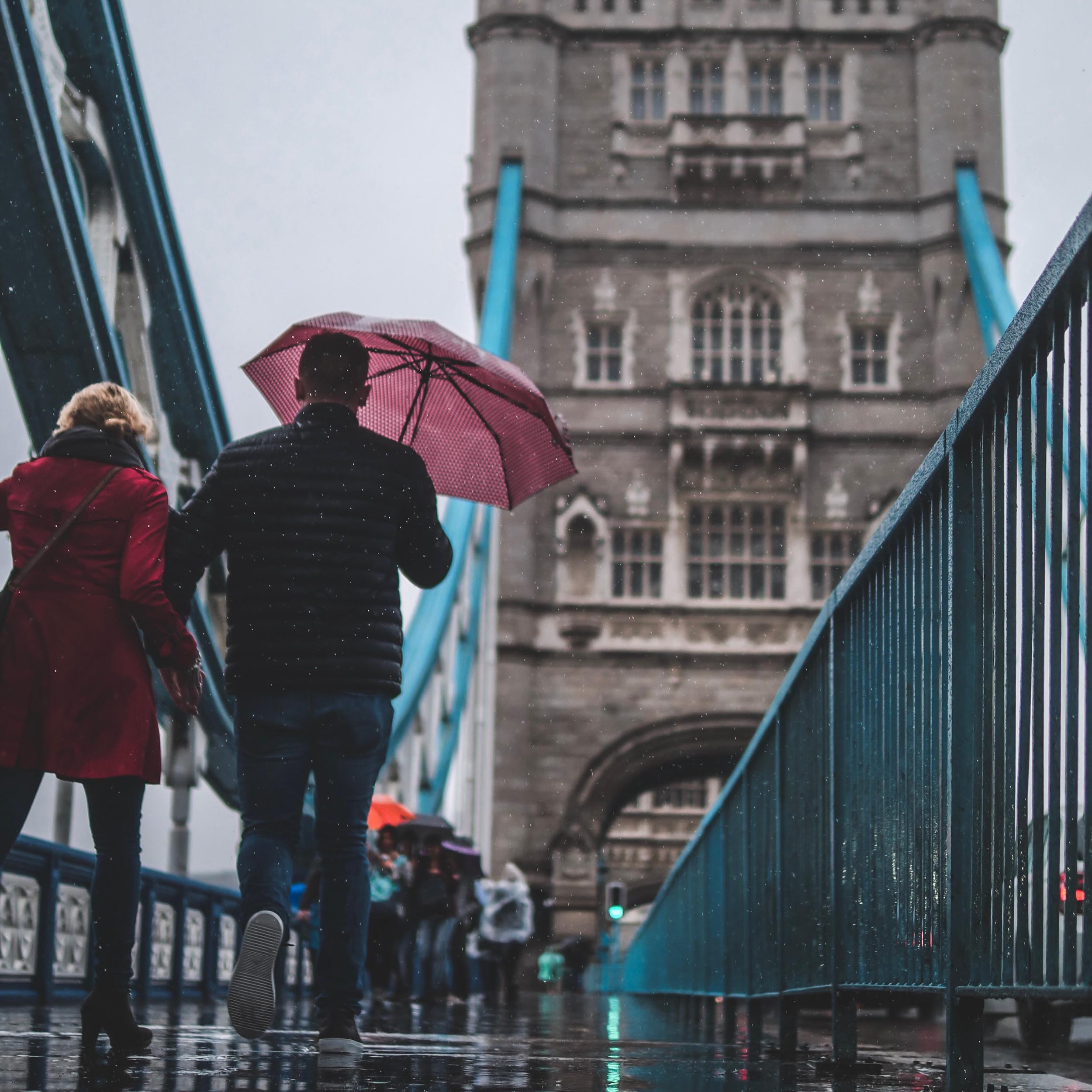 couple walking across a bridge in the rain holding an umbrella