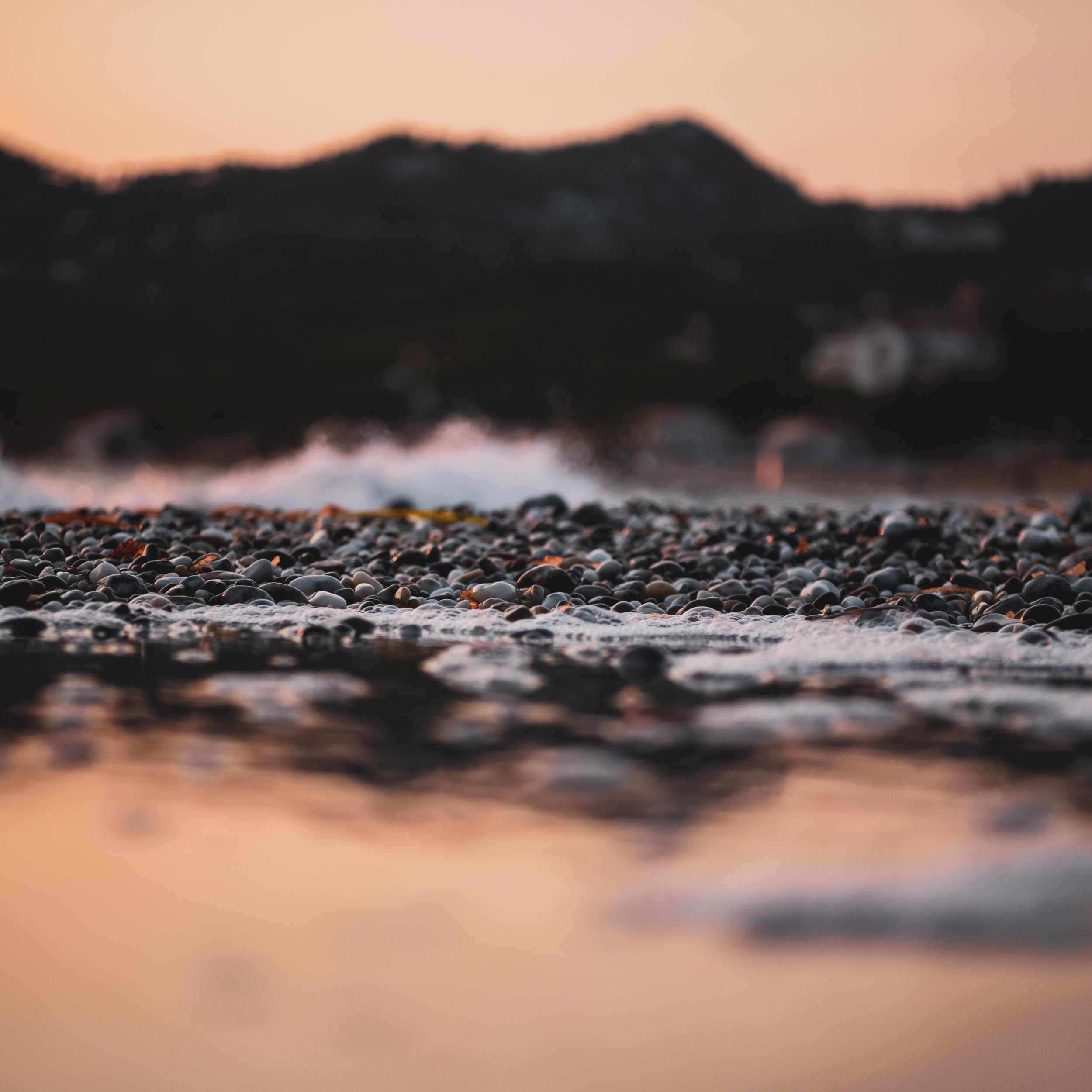 pebble beach with waves and mountains in the background