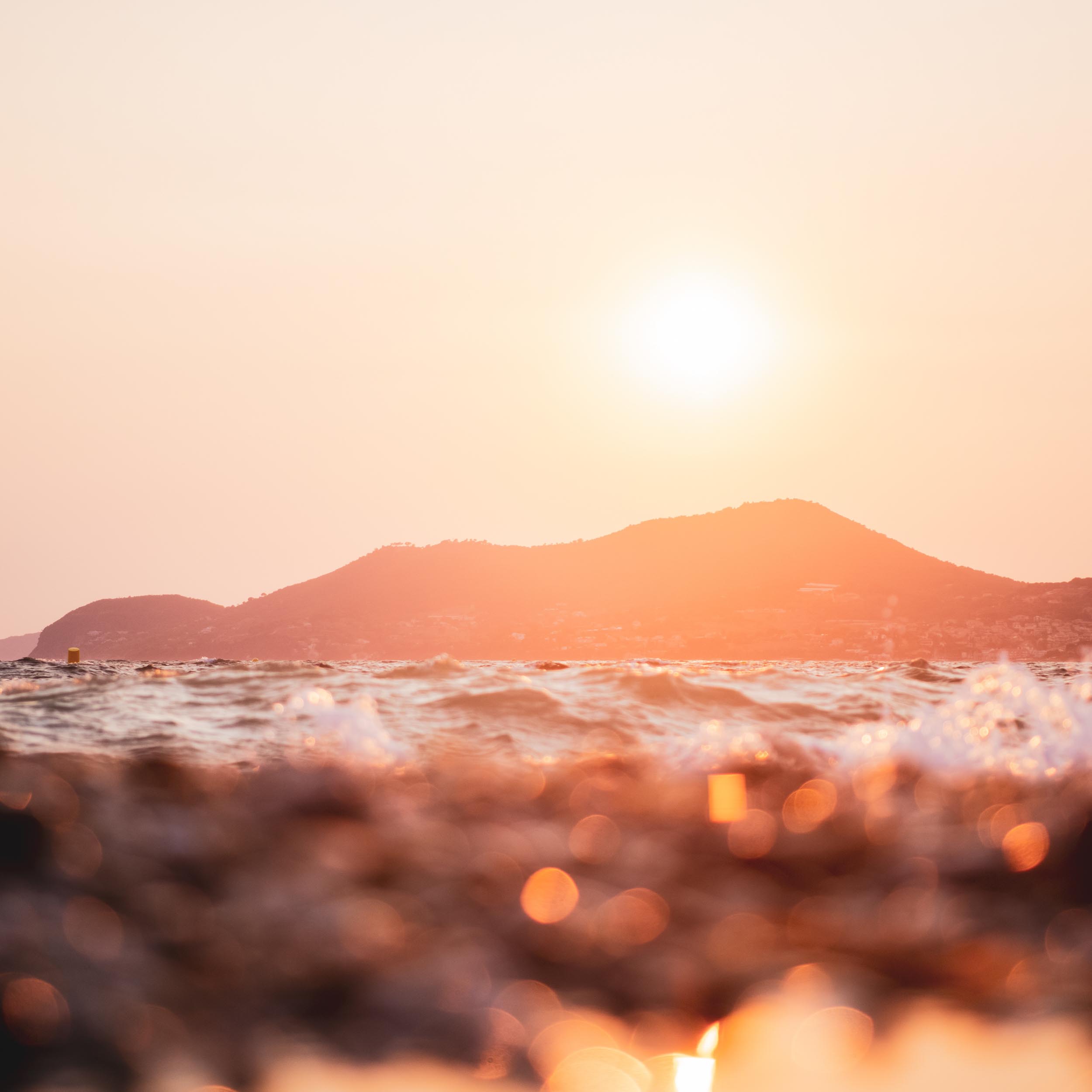sunset over the ocean with a mountain in the background